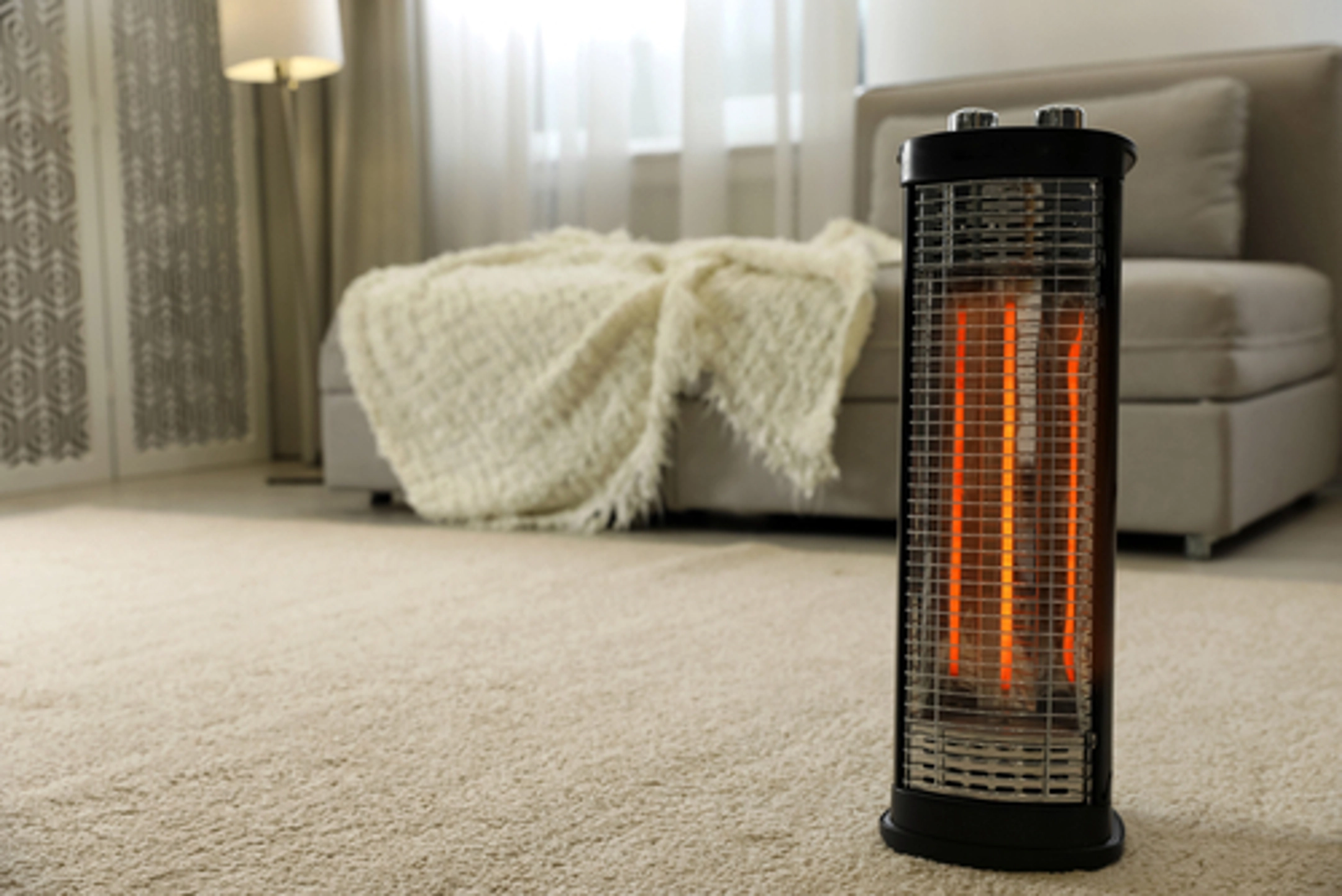 Tall black and orange space heater in an empty furnished room with tan couch and blanket in background