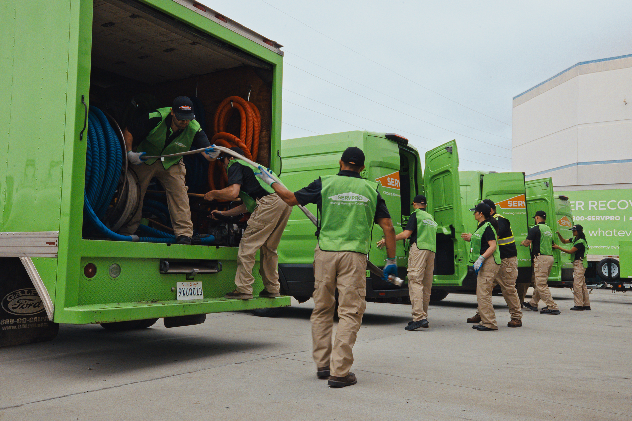 A team in green uniforms is unloading equipment from green service trucks in a parking area.