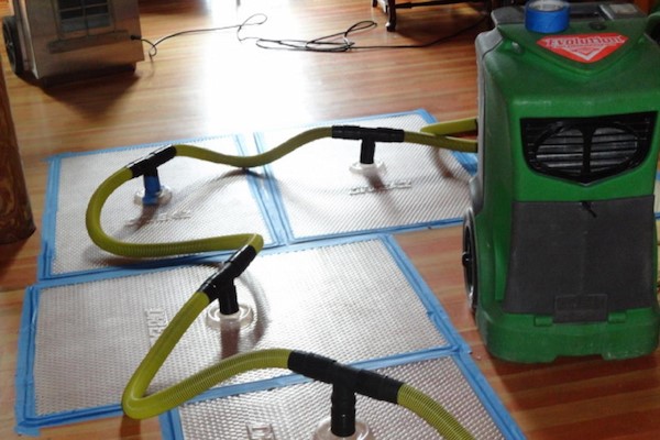 Water damage restoration equipment with drying mats and dehumidifier on hardwood floor