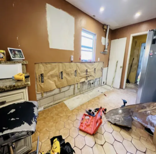 Kitchen interior showing active water damage restoration with stripped walls, exposed drywall repairs, and professional remediation equipment on site