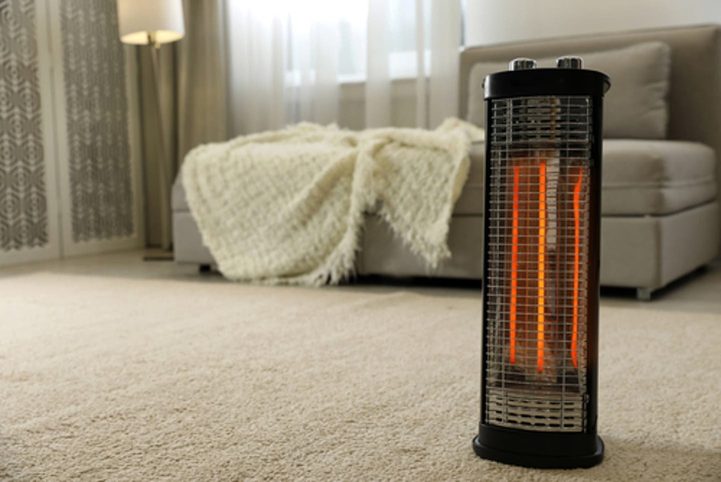 Tall black and orange space heater in an empty furnished room with tan couch and blanket in background