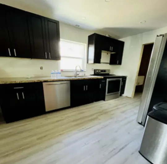 Fully restored kitchen after water damage remediation, featuring new dark cabinets, stainless steel appliances, granite countertops, and refinished light hardwood flooring